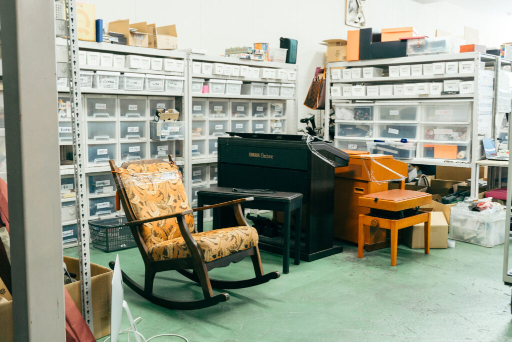 あきなやが買い取った物が置かれている倉庫の写真:ピアノや椅子などの大型家具から、香水、ゲームなどの小物まで